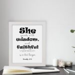 Proverbs 31:26 Bible wall art featuring bold and simple fonts on a white background, framed in black, highlighting the message of wisdom. displayed on the table in a white frame