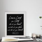 Matthew 22:37 Bible wall art with white text on a black background, reading Love the Lord your God with all your heart. displayed on the table in a white frame