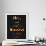 Ecclesiastes 3:11 wall art with golden text on a black background saying He Has Made Everything Beautiful In Its Time. displayed on the table in white frame