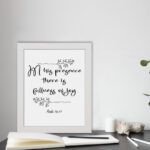 In His Presence There Is Fullness of Joy in a black script font with decorative branches and Psalm 16:11 on a white background - Christian wall art. displayed on the table in a white frame