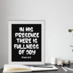 In His Presence There Is Fullness of Joy in bold white block letters with Psalm 16:11 on black background displayed on the table in a white frame - Christian wall art.