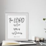 The Lord My God Lights Up My Darkness Psalm 18:28 white text on a black background with a black frame Christian wall art. displayed on the table in a white frame