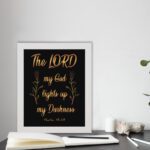 The Lord My God Lights Up My Darkness Psalm 18:28 gold text on black background Christian wall art displayed on the table in a white frame