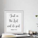 Trust In The Lord And Do Good Psalm 37:3 black cursive text on white background Christian wall art displayed on the table in a white frame