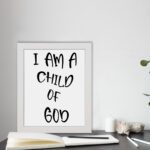 I Am a Child of God Bible wall art with bold black text on a white background, framed by a subtle black border. Wall Art displayed on the table in a white frame