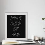 I Am A Child Of God Bible wall art with white handwritten text on a black background Wall Art displayed on the table in a white frame