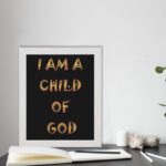 I Am A Child Of God Bible wall art with bold golden yellow text on a black background. Wall Art displayed on the table in a white frame