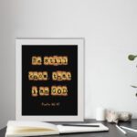 Be Still and Know That I Am God - Psalm 46:10 Bible Verse Wall Art with Scrabble-like Letters on Dark Background Wall Art displayed on the table in a white frame