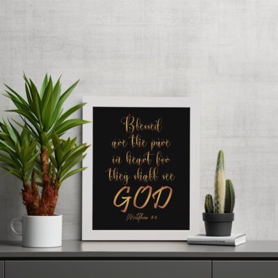 Infidu wall art with the text Blessed is the pure in heart, for they shall see God in gold font on a black background. displayed on the table in a white frame