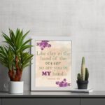 Infidu Jeremiah 18:6 Christian wall art with green and purple text on a light beige background, decorated with purple flowers in the corners. Wall Art displayed on the table in white frame