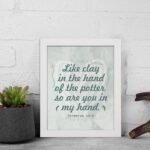 Infidu Jeremiah 18:6 Christian wall art with dark green cursive text on a light gray textured background, framed with decorative details. Wall Art displayed on the wall in a white frame