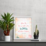 Infidu Isaiah 60:22 Christian wall art with coral and teal text, teal LORD, and a soft pastel watercolor background with floral shapes. Wall Art displayed on the table in a white frame