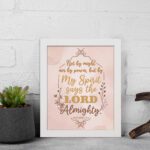 Zechariah 4:6 Christian wall art featuring Not By Might Nor By Power in gold script on a light peach background with floral accents. Wall Art kept on the wall in a white frame