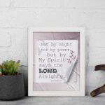 Zechariah 4:6 Bible verse wall art with soft purple text, bold LORD, decorative plant motif, and light purple folded paper background. displayed on the wall in a white frame