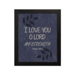 Bible verse wall art with Psalm 18:1 "I love you, O Lord, my strength" in white font on a Purple Blue Color background with a black leaf design and black frame hung on the wall.