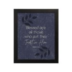 Christian wall art with Psalm 2:12 in white font on a purple-blue background with a black leaf design black frame hung on the wall.