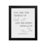 Christian wall art featuring the verse You Are The Temple Of God, His Spirit Dwells In You from 1 Corinthians 3:16 on a gray background with gray leaf design and black and gray font black frame hung on the wall.