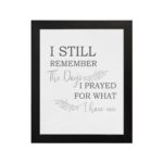 Christian wall art featuring the phrase I Still Remember The Days I Prayed For What I Have Now on a gray background with a gray leaf design and black and gray font black frame hung on the wall.