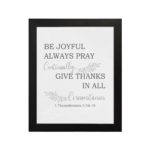 Christian wall art featuring 1 Thessalonians 5:16-18 Bible verse on a white background with gray leaf design and black font and black frame hung on the wall