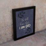 Purple-blue background with black leaf design, white text Be Still Know That I Am God Psalm 46:10 Bible Verse Wall Art black frame on the wall.