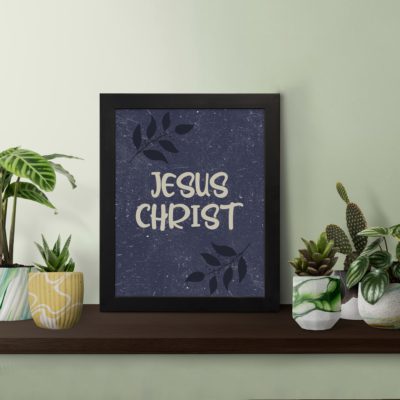 Christian wall art with purple-blue background, black leaf design, and white text Infidu Jesus Christ Bible Verse Wall Art white frame displayed on the table