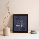 Purple-blue background with black leaf design, white text Be Still Know That I Am God Psalm 46:10 Bible Verse Wall Art black frame displayed on the wall.