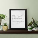 Gray background with leaf design, black and gray text 'For With God Nothing Shall Be Impossible Luke 1:37 Bible Verse Wall Art black frame displayed on the table