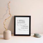 Christian wall art featuring the phrase I Still Remember The Days I Prayed For What I Have Now on a gray background with a gray leaf design and black and gray font black frame displayed on the wall.