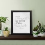 Christian wall art featuring Psalm 56:4 Bible verse on a gray background with gray leaf design and black and gray font black frame on the table.