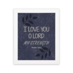 Bible verse wall art with Psalm 18:1 "I love you, O Lord, my strength" in white font on a Purple Blue Color background with a black leaf design and white frame hung on the wall.