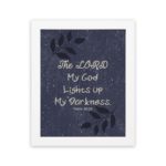 Purple-blue background with black leaf design, white text 'The Lord My God Lights Up My Darkness Psalm 18:28 Bible Verse Wall Art white frame hung on the wall.