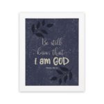 Purple-blue background with black leaf design, white text Be Still Know That I Am God Psalm 46:10 Bible Verse Wall Art white frame hung on the wall.