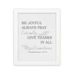 Christian wall art featuring 1 Thessalonians 5:16-18 Bible verse on a white background with gray leaf design and black font and white frame hung on the wall