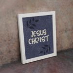 Christian wall art with purple-blue background, black leaf design, and white text Infidu Jesus Christ Bible Verse Wall Art white frame on the wall