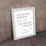 Christian wall art featuring the verse You Are The Temple Of God, His Spirit Dwells In You from 1 Corinthians 3:16 on a gray background with gray leaf design and black and gray font white frame on the wall.