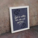 Christian wall art with purple-blue background, black leaf design, and white text God Is Within Her She Will Not Fall Psalm 46:5 Bible Verse Wall Art white frame on the wall