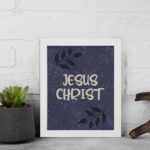 Christian wall art with purple-blue background, black leaf design, and white text Infidu Jesus Christ Bible Verse Wall Art white frame displayed on the wall