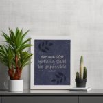 Christian wall art with purple-blue background, black leaf design, and white text For With God Nothing Shall Be Impossible Luke 1:37 Bible Verse Wall Art white frame displayed on the table