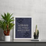 Purple-blue background with black leaf design, white text 'With God All Things Are Possible Matthew 19:26 Bible Verse Wall Art white frame on the table