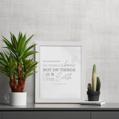 Gray background with leaf design, black and gray text 'Set Your Affection On Things Above Colossians 3:2 Bible Verse Wall Art and black frame displayed on the table