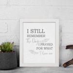 Christian wall art featuring the phrase I Still Remember The Days I Prayed For What I Have Now on a gray background with a gray leaf design and black and gray font white frame displayed on the wall.