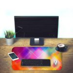 Infidu Geometric Patterns Desk Pad with overlapping transparent diamond shapes in multi-colored gradients. Desk Pad with Keyboard and Mouse on the table