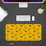 Desk pad with a bright yellow background featuring black curved lines and blue circular shapes. Desk Pad kept on a gray background