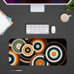 Infidu Artistic Desk Mat with concentric orange and white circular patterns on a dark blue or black background. Desk Pad with Design Kept on a computer table