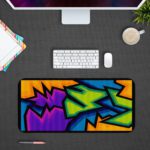 Infidu Artistic Patterns Desk Mat with sharp, angular shapes in purple, blue, green, orange, and black resembling graffiti. Desk Pad with Design Kept on a computer table