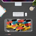 Infidu Artistic Patterns Desk Pad with bold, brushstroke-like shapes in yellow, black, red, and white on a gray background. Desk Pad with Design Kept on a computer table