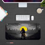 Infidu Artistic Desk Pad with a shadowy anthropomorphic cat or wolf riding a bicycle against a city skyline and a large yellow moon. Design Kept on a computer table