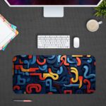 Infidu Desk Pad with a funky pattern of abstract curved shapes in blue, red, and yellow. Design Kept on a computer table