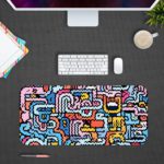 Colorful abstract maze design desk pad with wavy lines in blue, pink, yellow, white, and black on a light blue background. Design Kept on a computer table