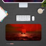 Infidu desk pad featuring a small boat on a red ocean under a red sky, capturing a serene sunrise or sunset scene. Design Kept on a computer table